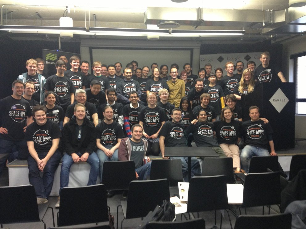 Group of Space Apps participants in a room together posing for a picture wearing black Space Apps t-shirts